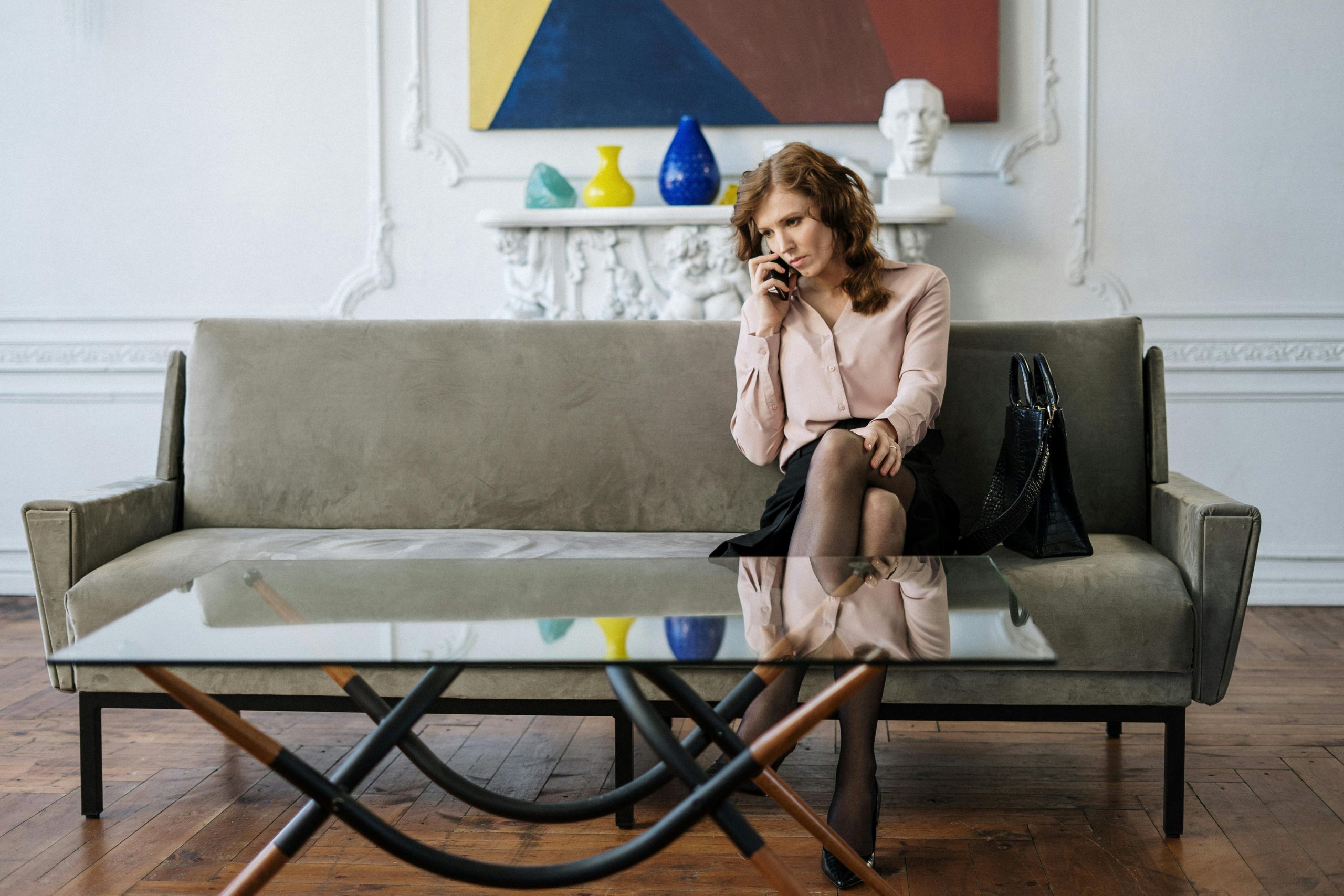 A woman sits thoughtfully on a sofa, engaged in a phone call in a stylish living room.